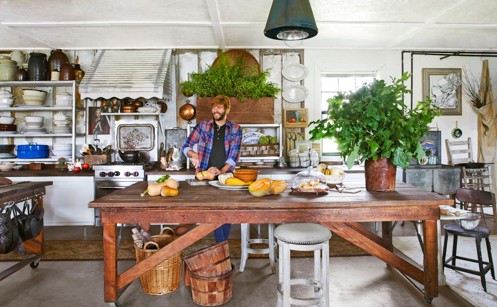 a man in a plaid shirt cuts vegetables at an oversize work table in a country kitchen