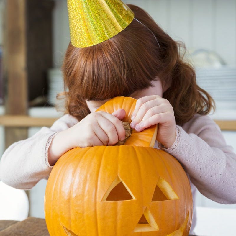 halloween trivia girl lifting the top of a carved pumpkin to peek inside