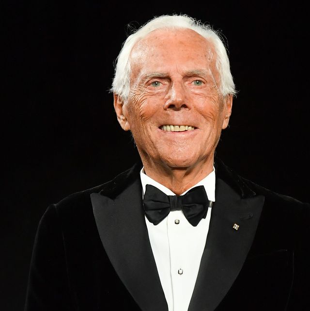 a man smiles while standing in a black tuxedo with a white shirt