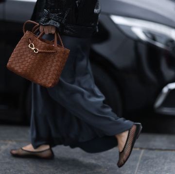 a woman carrying a brown leather andiamo tote bag by bottega veneta with a black jacket and silk skirt on the sidewalk in paris in a roundup of the best small tote bags 2024