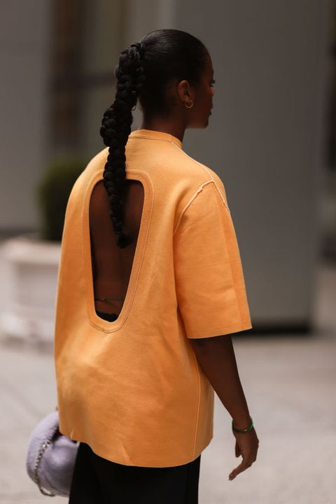 a woman wearing an oversize orange shirt with a back cutout and purple bag on the street during new york fashion week in a roundup of cute summer outfits 2023