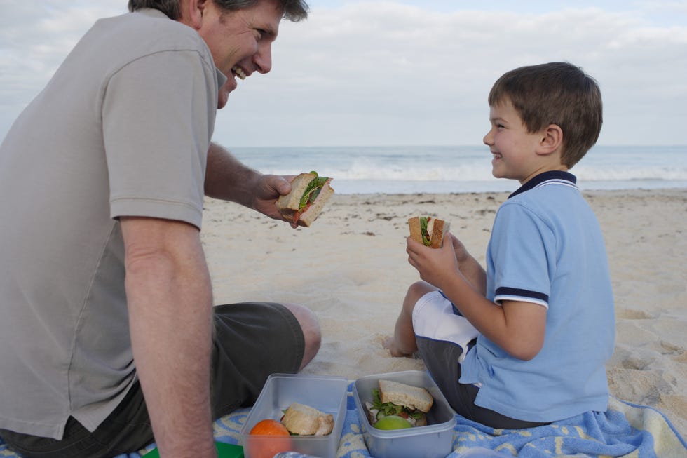 un padre y su hijo se comen un sandwich en la playa