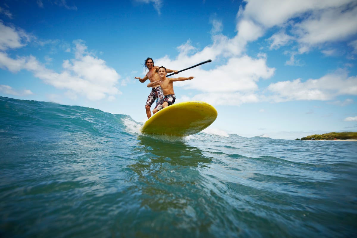 father and son riding wave on stand up paddleboard