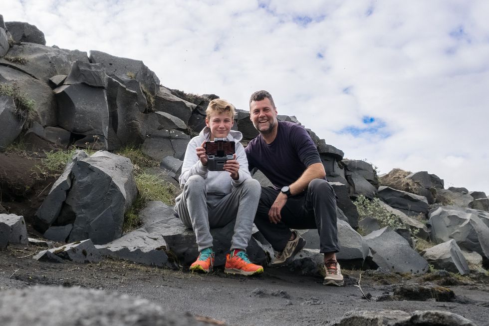 father and son drone selfie with boy sitting on rocks