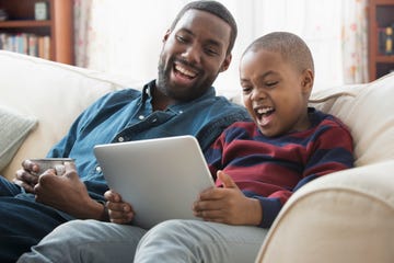 father and son using digital tablet on sofa