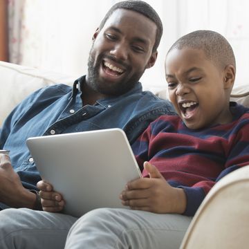 father and son using digital tablet on sofa
