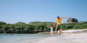 father and young daughter jumping on tropical beach, miyakojima island, japan