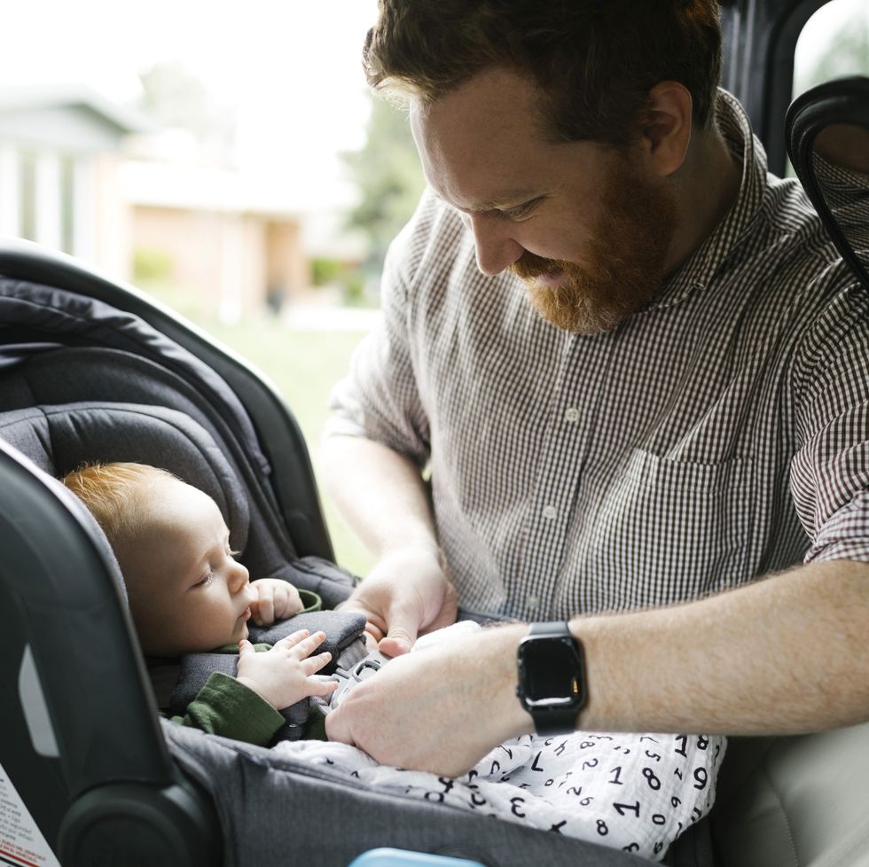 father buckling baby boy 2 3 months in car seat