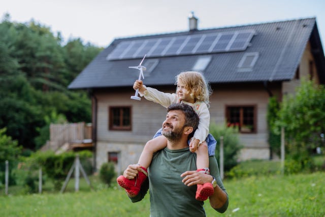padre con su hijo en hombros en una casa de campo con paneles solares