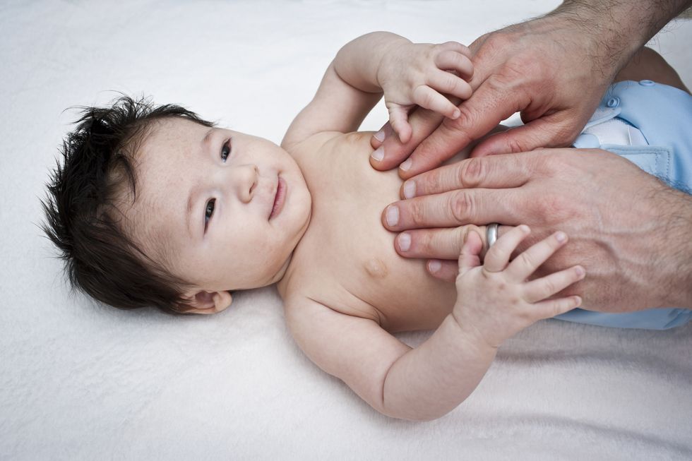 un niño de cuatro meses recibe un masaje en el estómago por parte de su padre