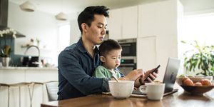 father multi tasking with young son 2 yrs at kitchen table