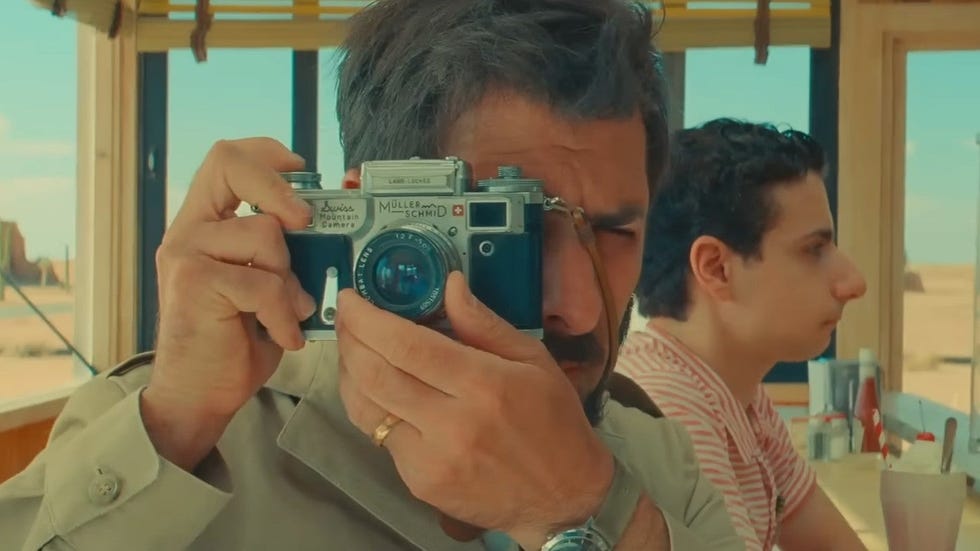 a man takes a photo with a film camera in a scene from asteroid city