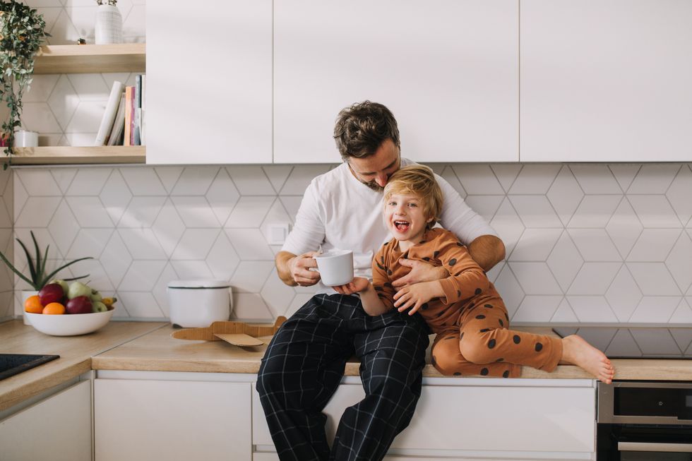 father sitting on kitchen counter with his little son and having morning coffee