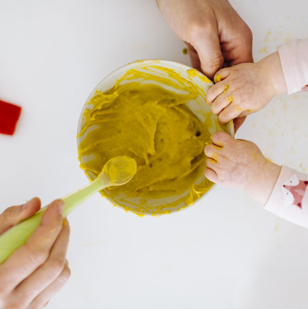 father with spoon and baby girl touching bowl with baby food