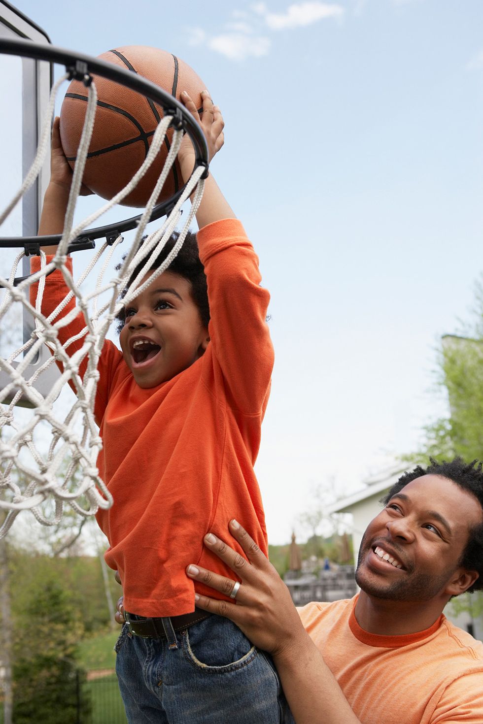 father holding his toddler son up to basketball hoop so he can dunk