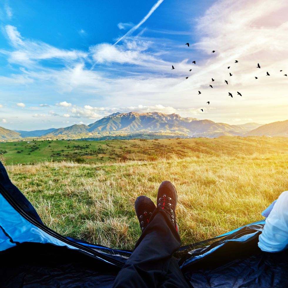 person overlooking nature with feet hanging out of tent while camping