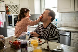 toddler girl feeding her father a strawberry in the kitchen