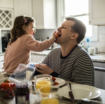 toddler girl feeding her father a strawberry in the kitchen