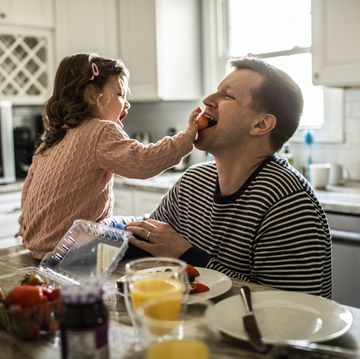 toddler girl feeding her father a strawberry in the kitchen