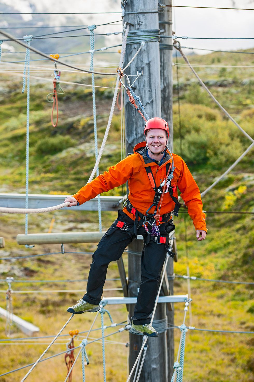 man in orange jacket balancing on a ropes course