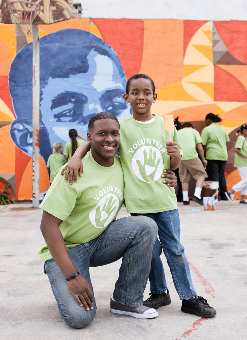 father and son in green volunteer shirts in front of a painted mural