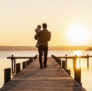 a father holding a baby is walking down a dock at sunset