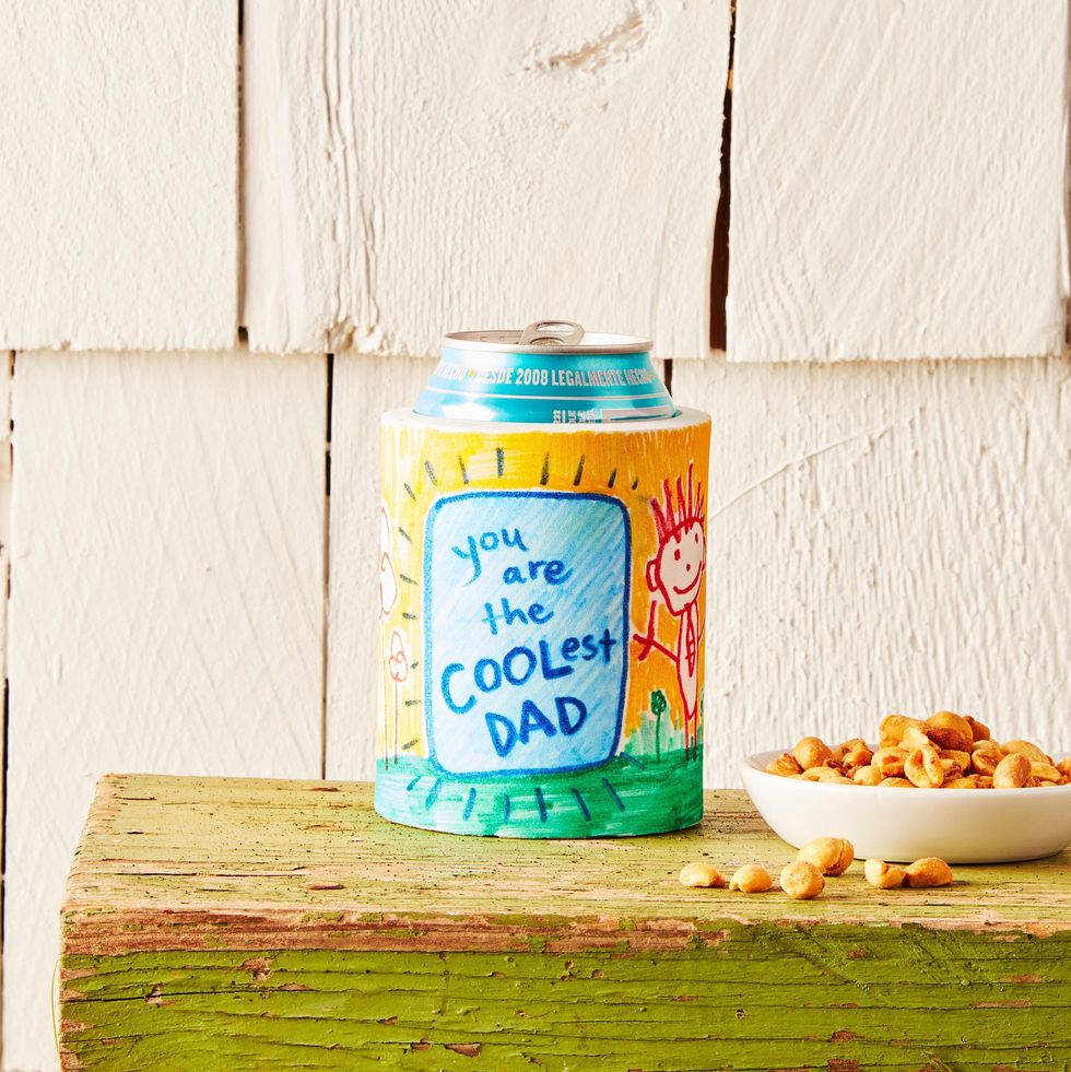 drink koozie father's day craft decorated with child's drawing and the words you are the coolest dad, shown on a green painted bench beside a bowl of peanuts