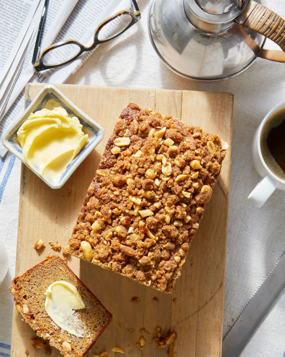 banana bread with salted peanut streusel on a cutting board with a cup of coffee