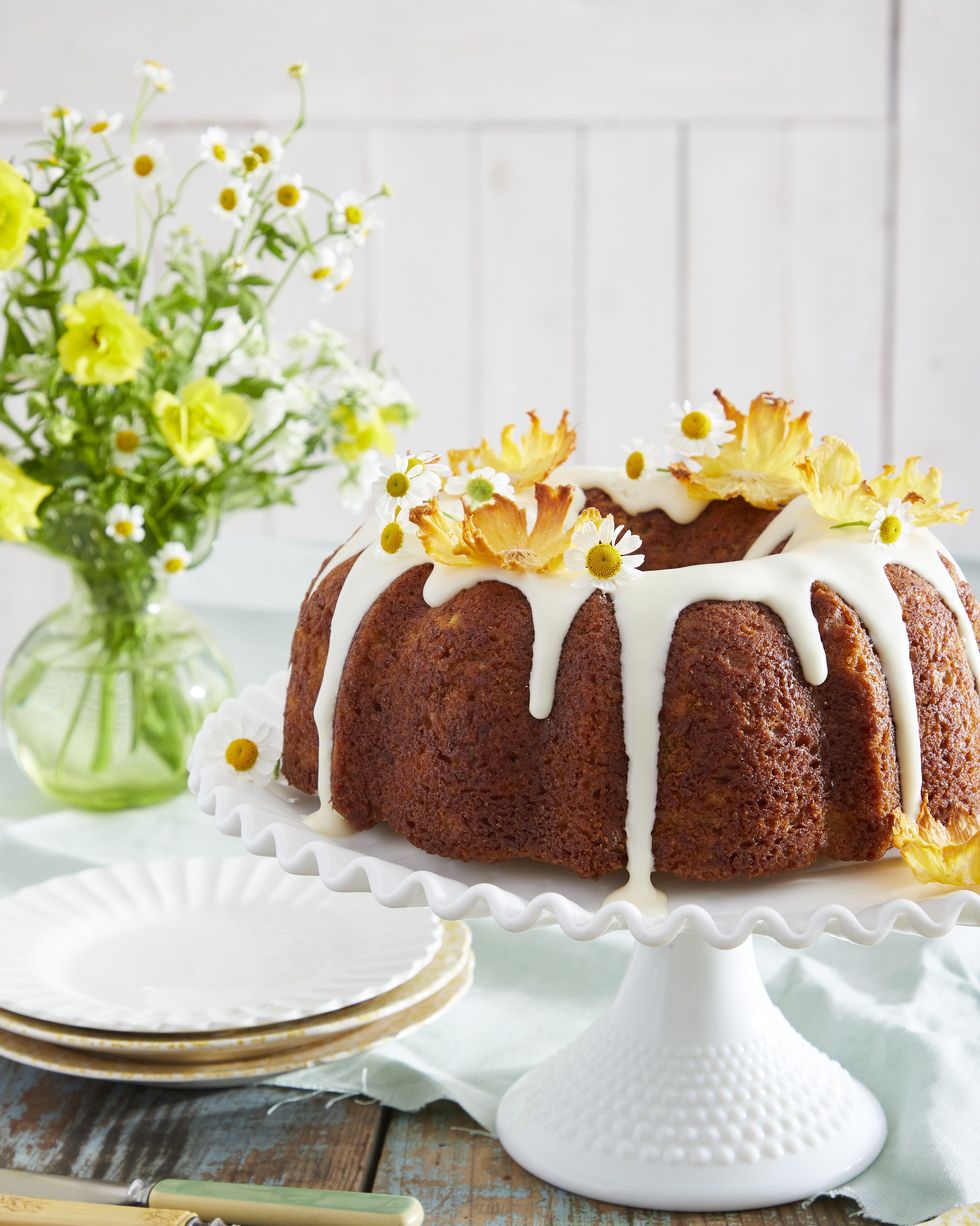 hummingbird bundt cake on a white cake stand and topped with a cream cheese glaze and pineapple flowers