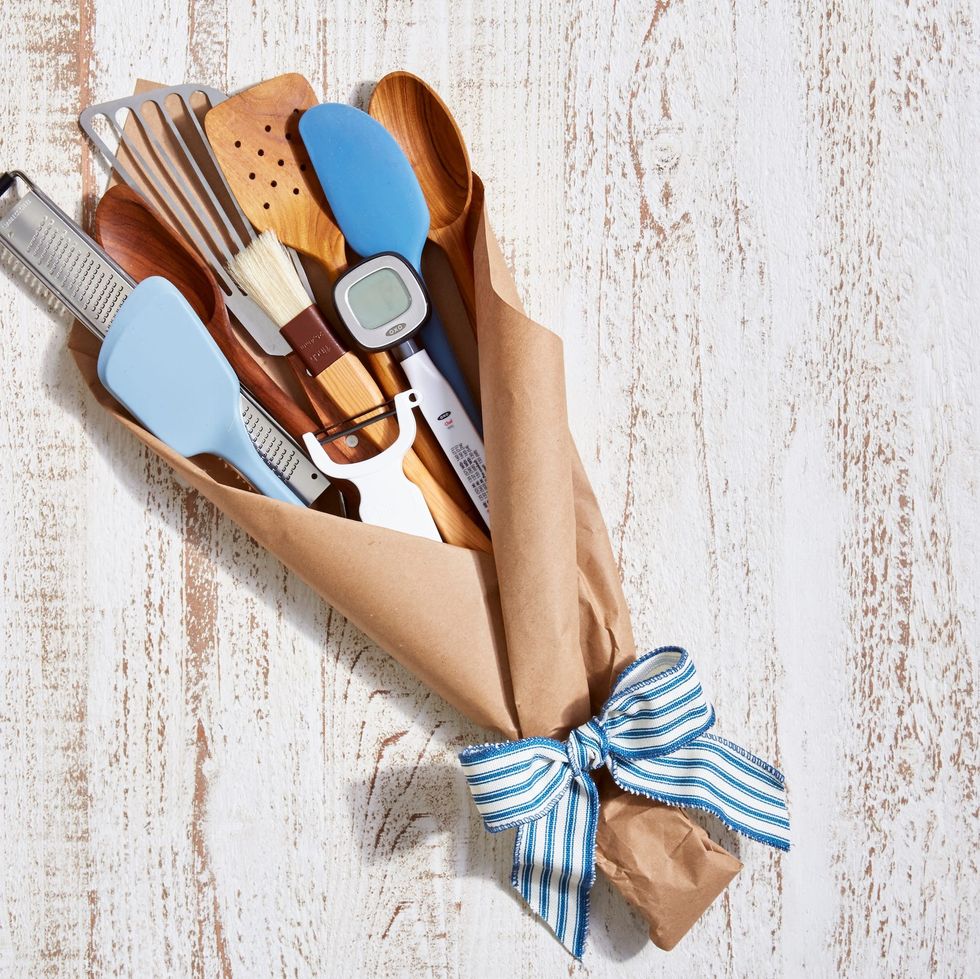 kitchen spatulas, thermometer, and microplane grater wrapped in brown craft paper and tied with blue and white stripe ribbon to resemble a bouquet for a fathers day gift basket