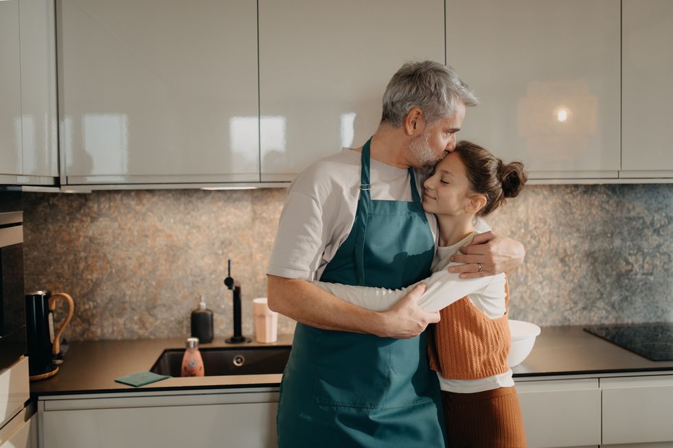 mature man with his teen daughter embracing in kitchen