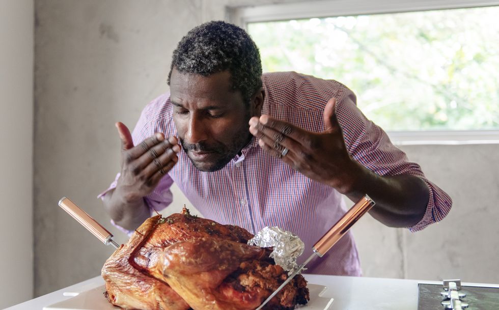 man taking a deep whiff of a roasted thanksgiving turkey, using both hands to wave the aroma toward his nose