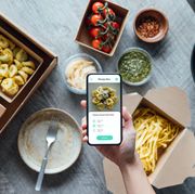 meal delivery app on smartphone and preparing ingredients for cooking   with ravioli, pasta, tomato, cheese, pesto sauce and spices