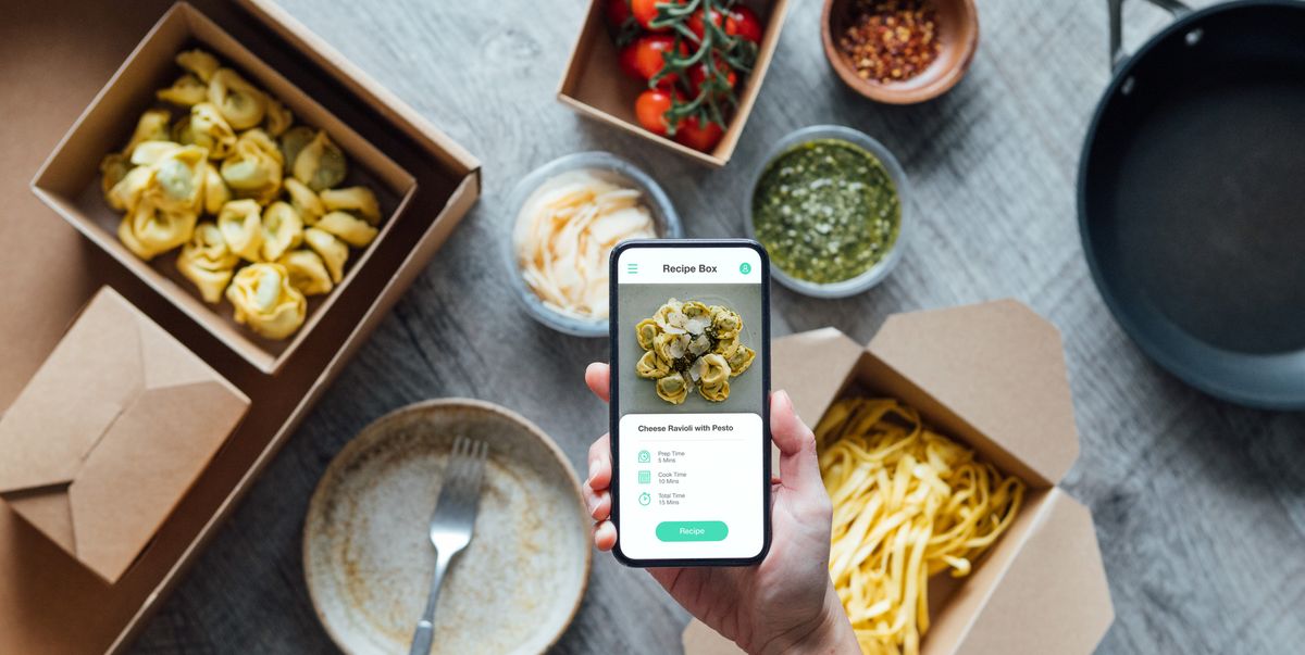 meal delivery app on smartphone and preparing ingredients for cooking   with ravioli, pasta, tomato, cheese, pesto sauce and spices