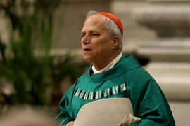 a man in green robes and a red head covering stands and looks to the right