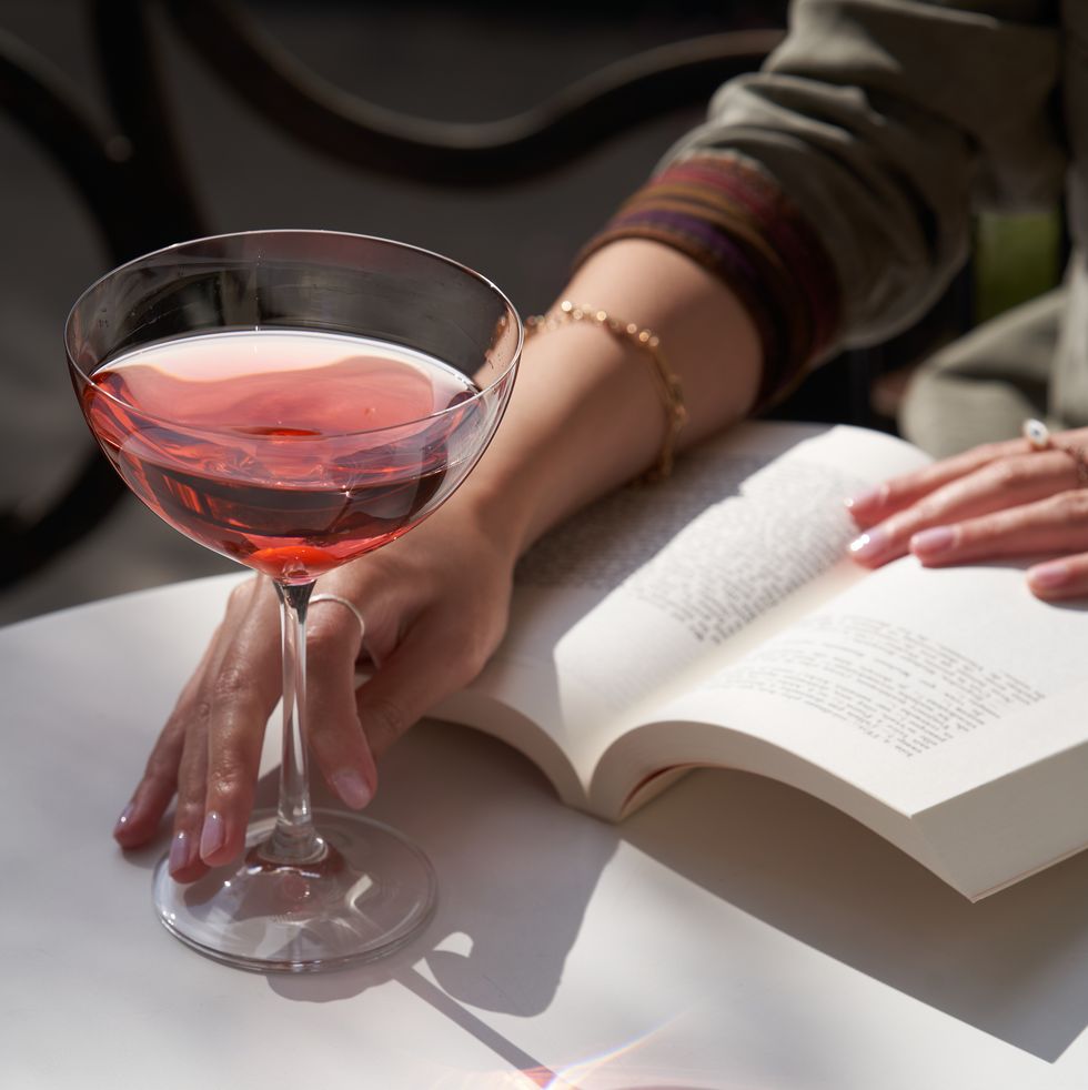 woman reads a book and has a red cocktail in martini glass beside her