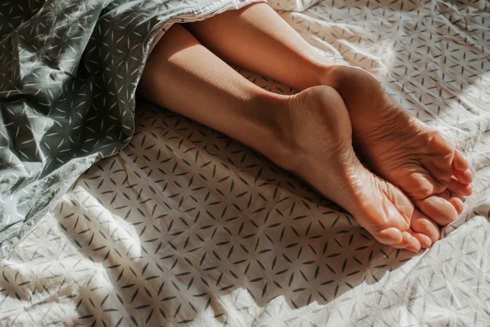 feet of woman peeking out from under the covers girl alone sleep in bed wake up female legs happy morning in bedroom cozy and comfortable sunlight on bed linen pillow, blanket recovery, relax