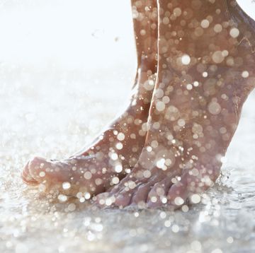 primer plano de los pies de una mujer en la orilla de una playa con gotas de agua