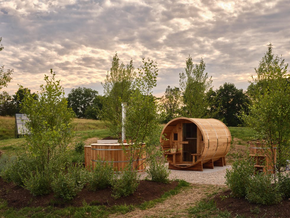 Outdoor wellness area with wooden barrel sauna and hot tub surrounded by greenery.