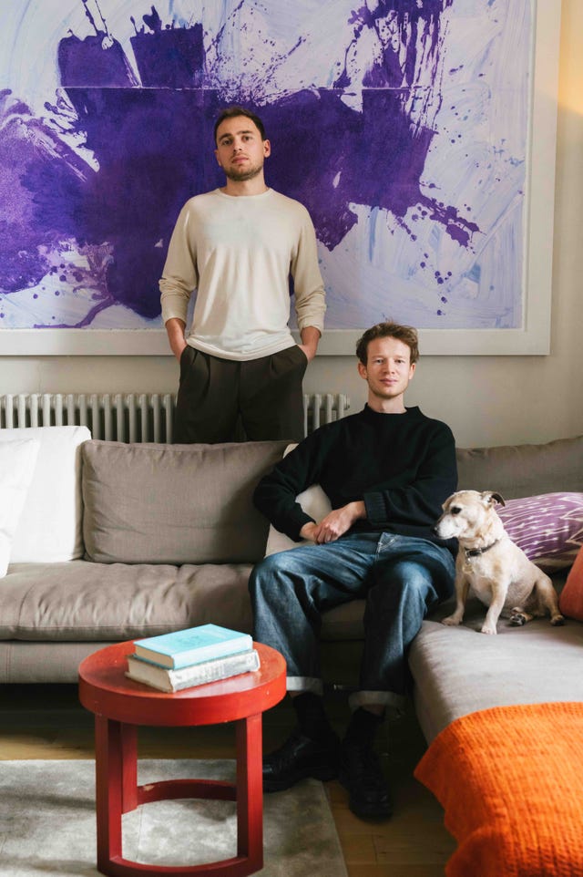two men in a living room with a dog