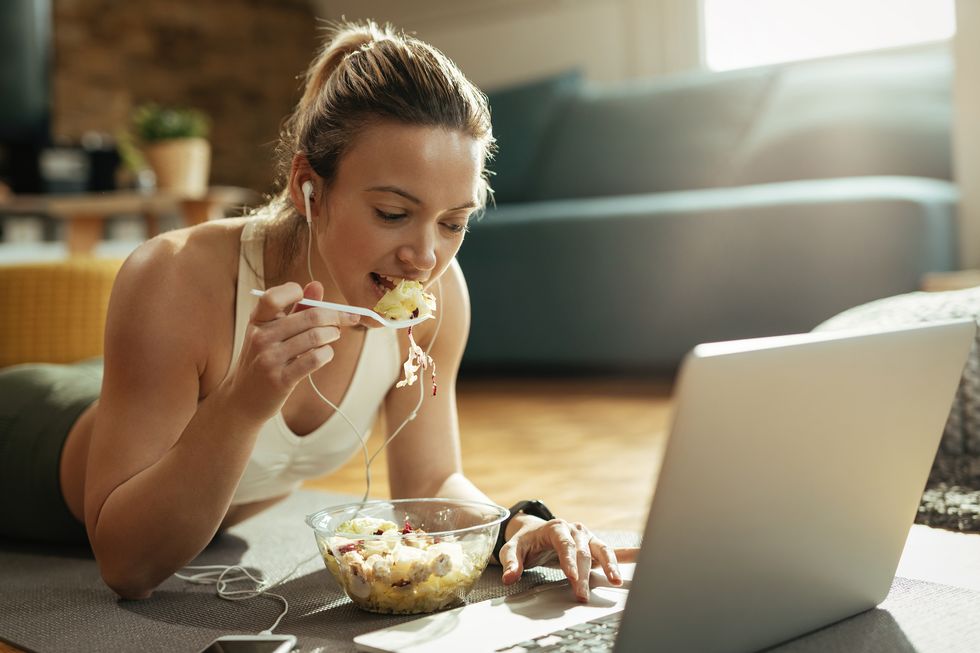 female athlete eating salad and using laptop while relaxing at home