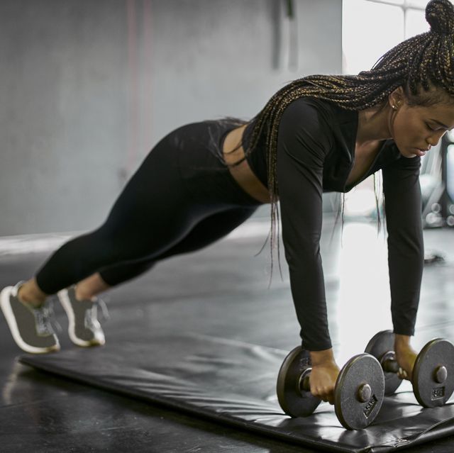 female athlete with braided hair holding dumbbells while exercising on mat in gym