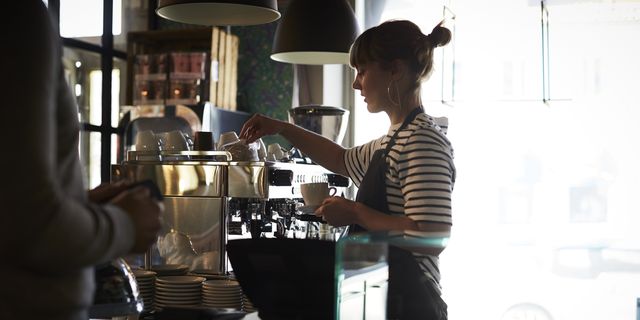Female barista preparing coffee while customer standing at checkout counter