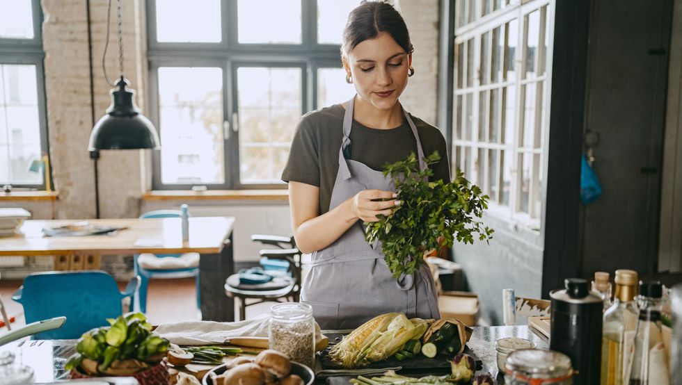 female chef wearing apron doing quality check of cilantro standing in studio kitchen