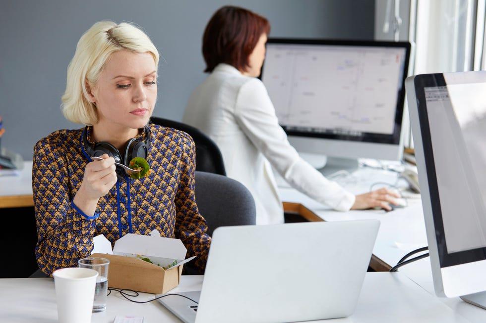 Female designer looking at laptop during working lunch at office desk