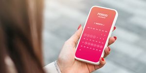 female hand holding a mobile phone with an open menstrual cycle calendar application
