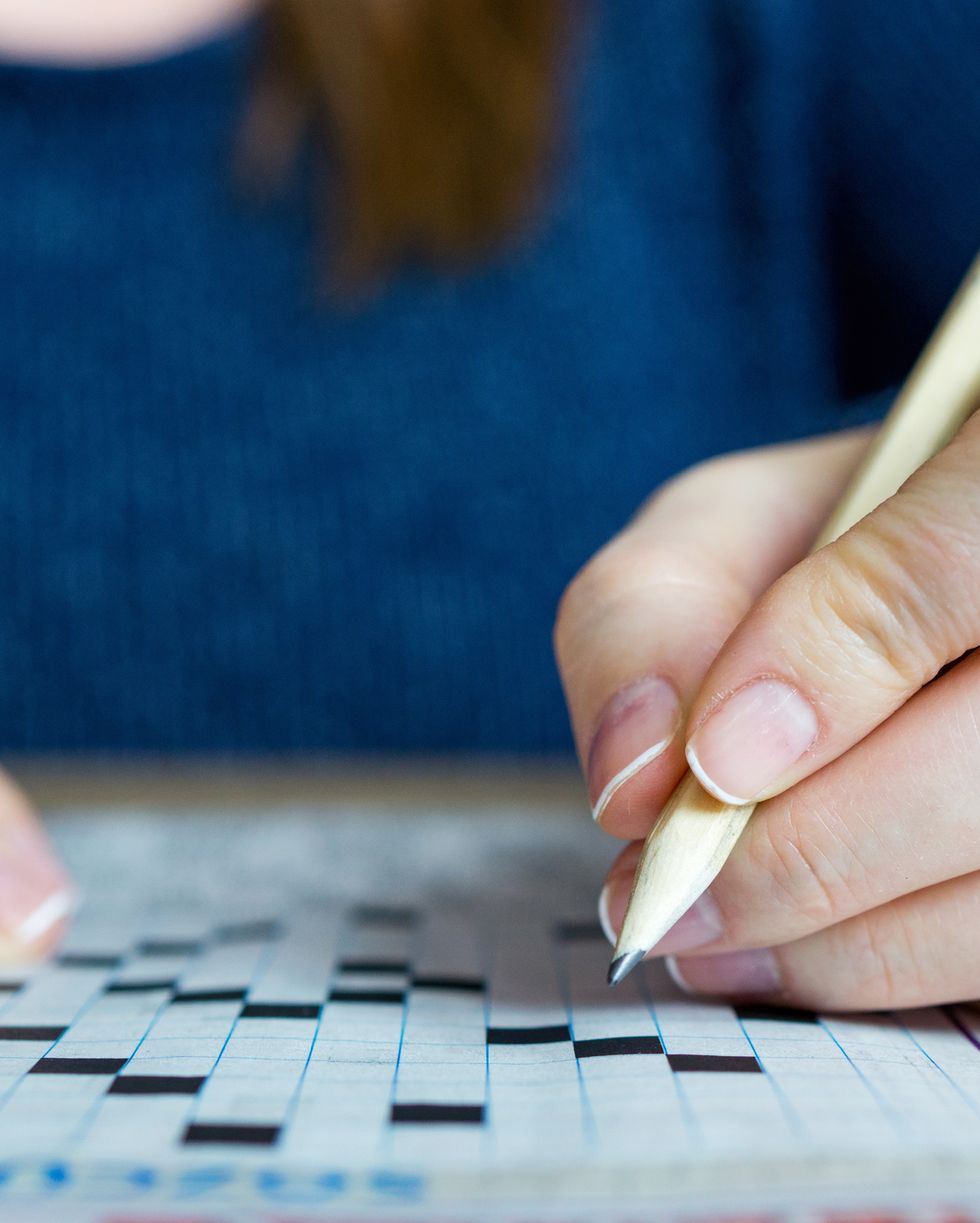 Female hand holding a pencil and solves crossword puzzle