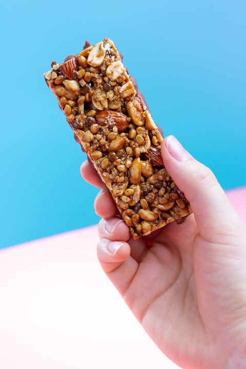 female hand holding a protein bar on a blue and pink background