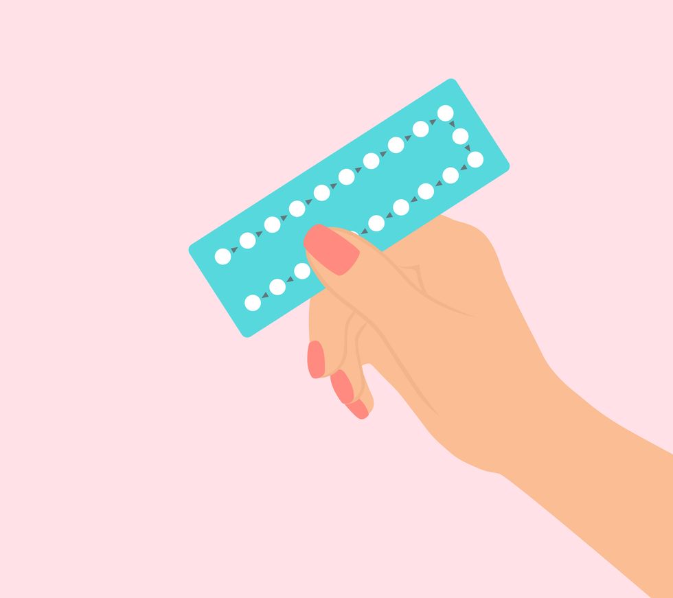 female hand holding birth control pills on pink background