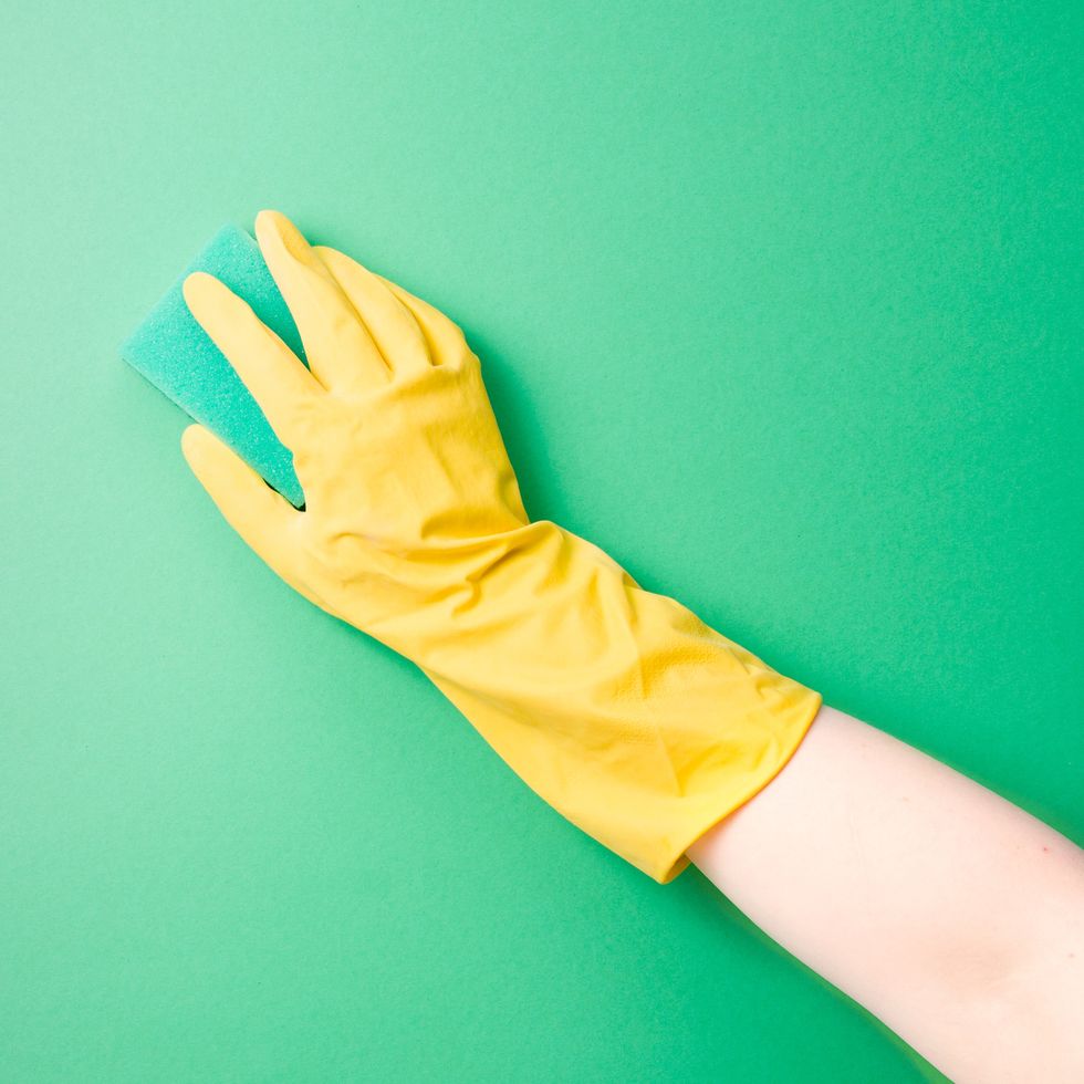 a female hand in a yellow rubber glove washes a plain surface with a green paralon sponge